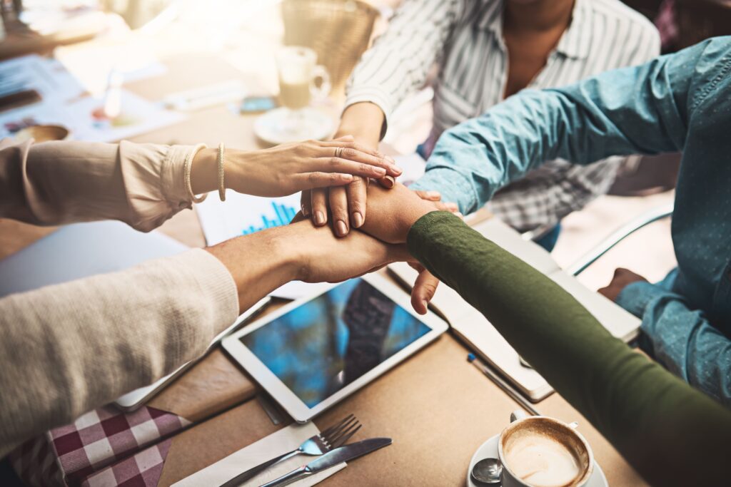 Diverse team joining hands in a collaborative workspace to foster innovation and community.